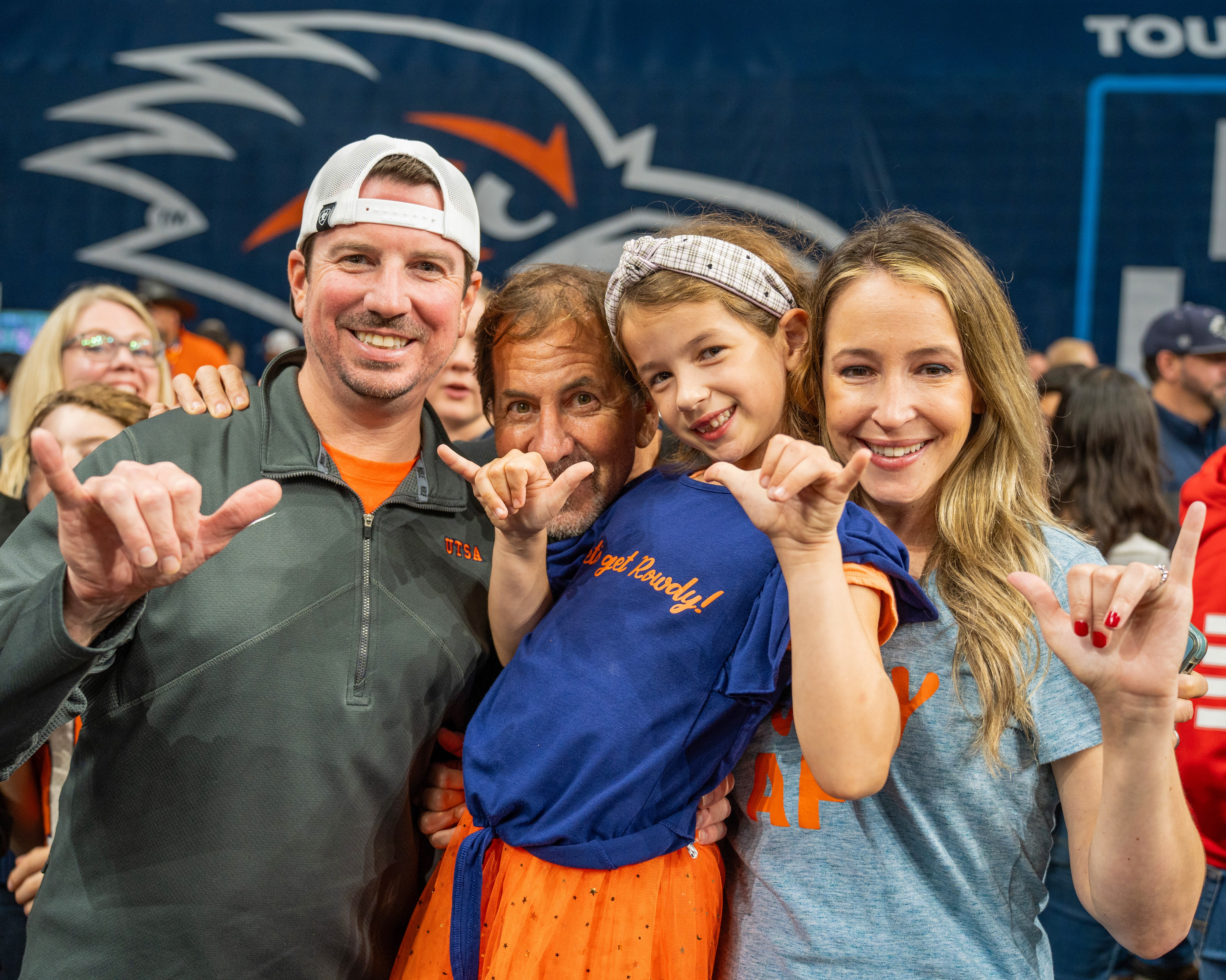 Picture of family from left to right father with a white hat, grandfather, young daughter, and mother all holding the "UTSA Birds Up" hand gesture.